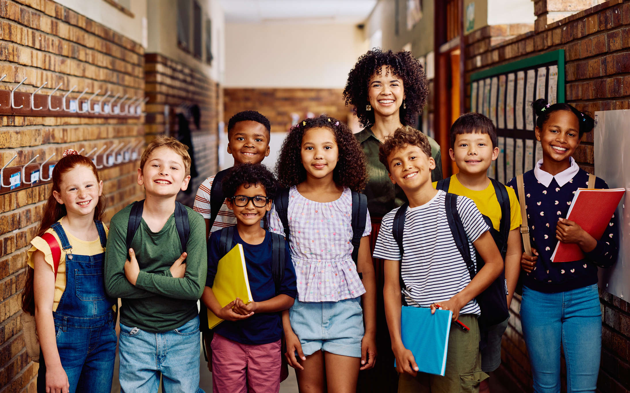 Portrait of multiracial elementary school children and young female teacher smiling at camera in school corridor stock photo